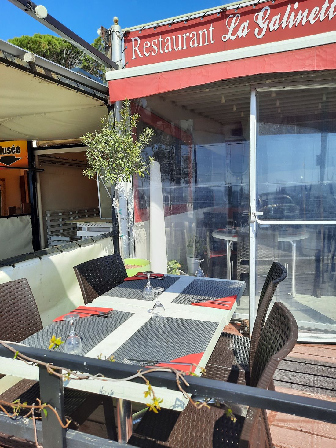 La terrasse du restaurant sous son auvent rouge portant l'enseigne « Restaurant La Galinette », tables dressées