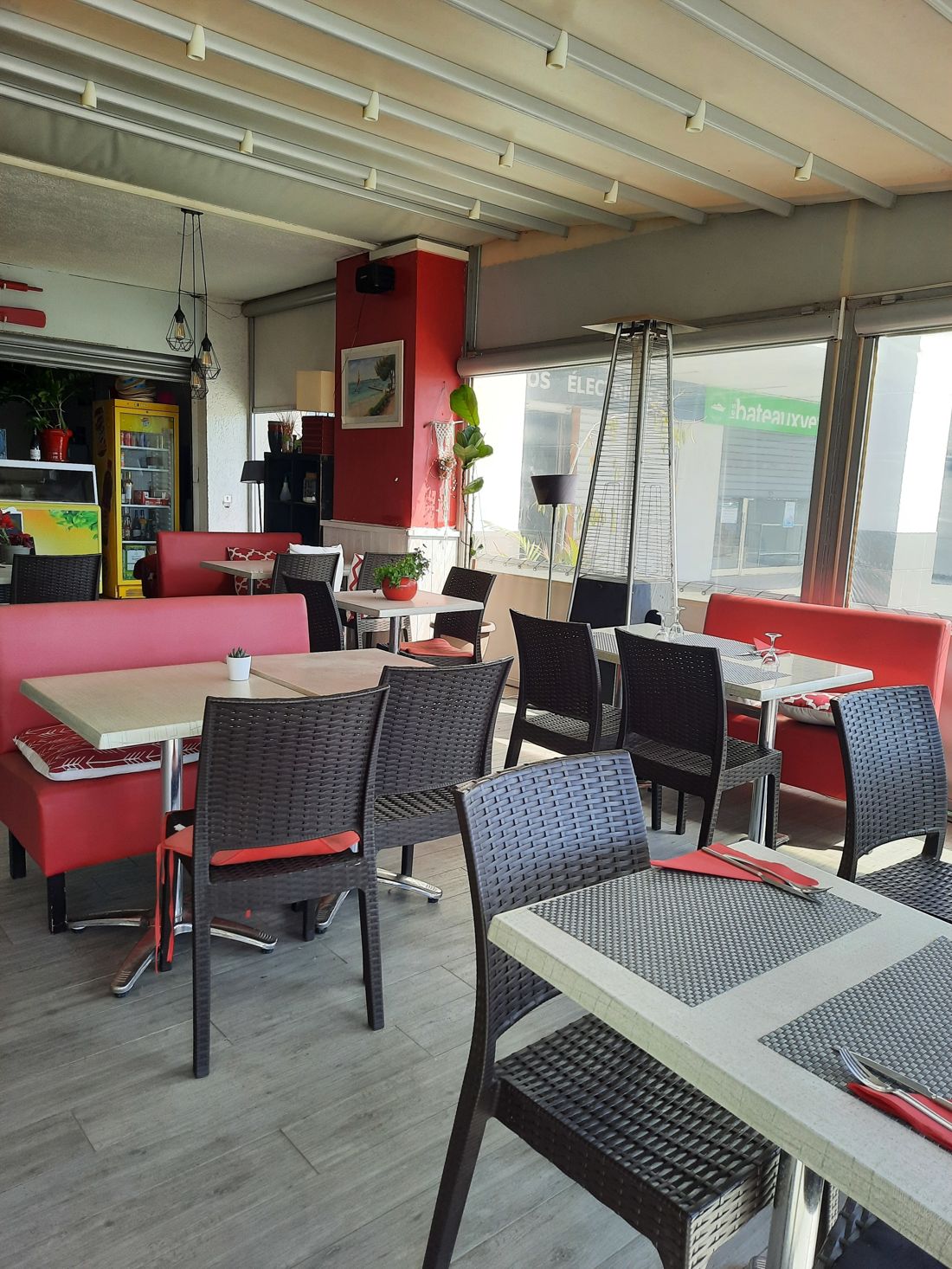La salle : banquettes rouges, tables claires, chaises tressées et suspensions